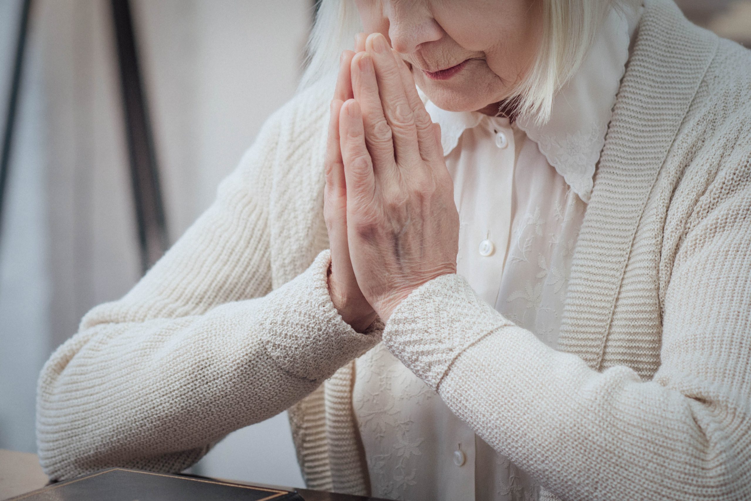 .אישה יושבת ומצמידה את שתי ידייה בצורת תפילה, אל מול ספר תפילה