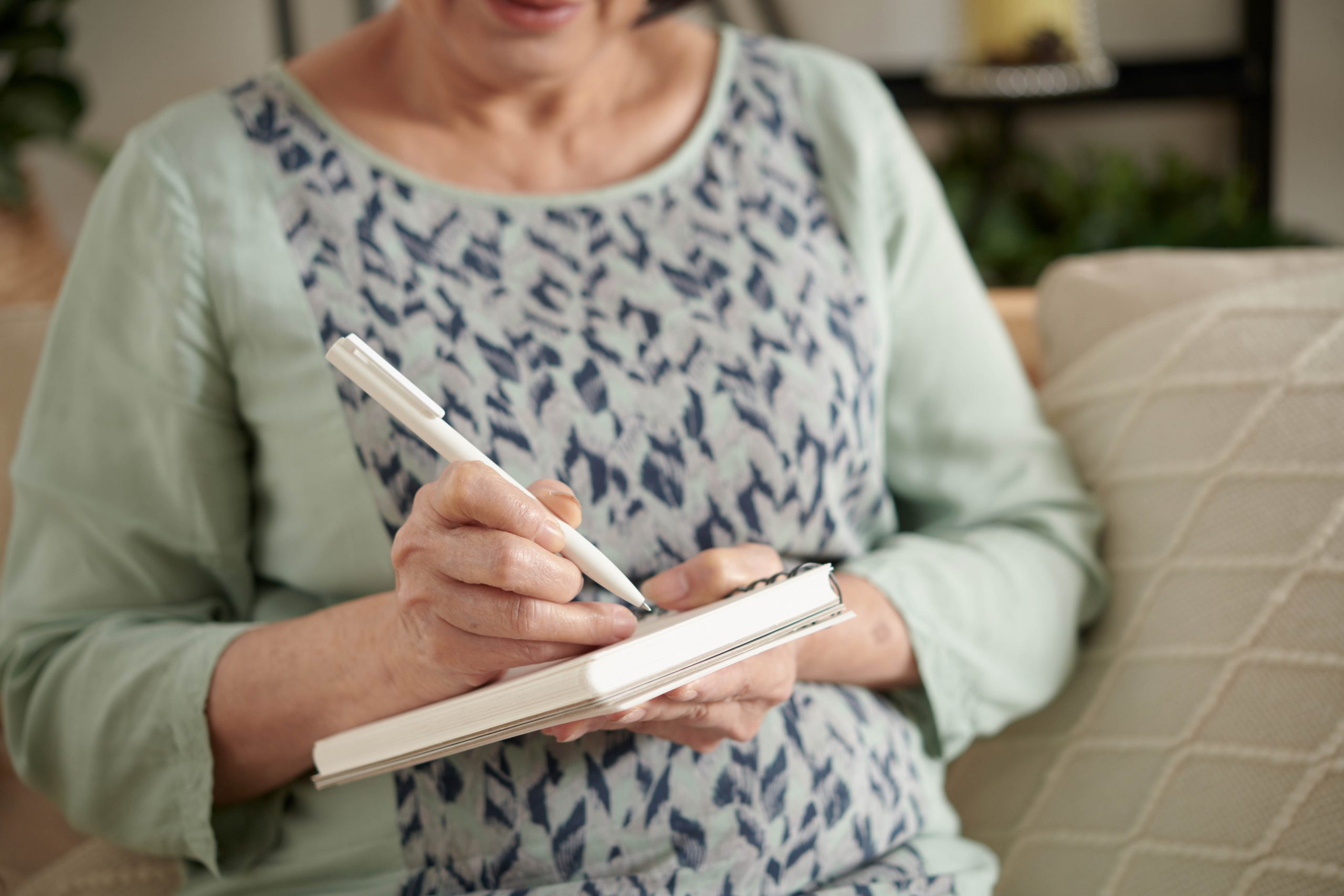 .אישה יושבת על ספה, מחזיקה מחברת ועט וכותבת