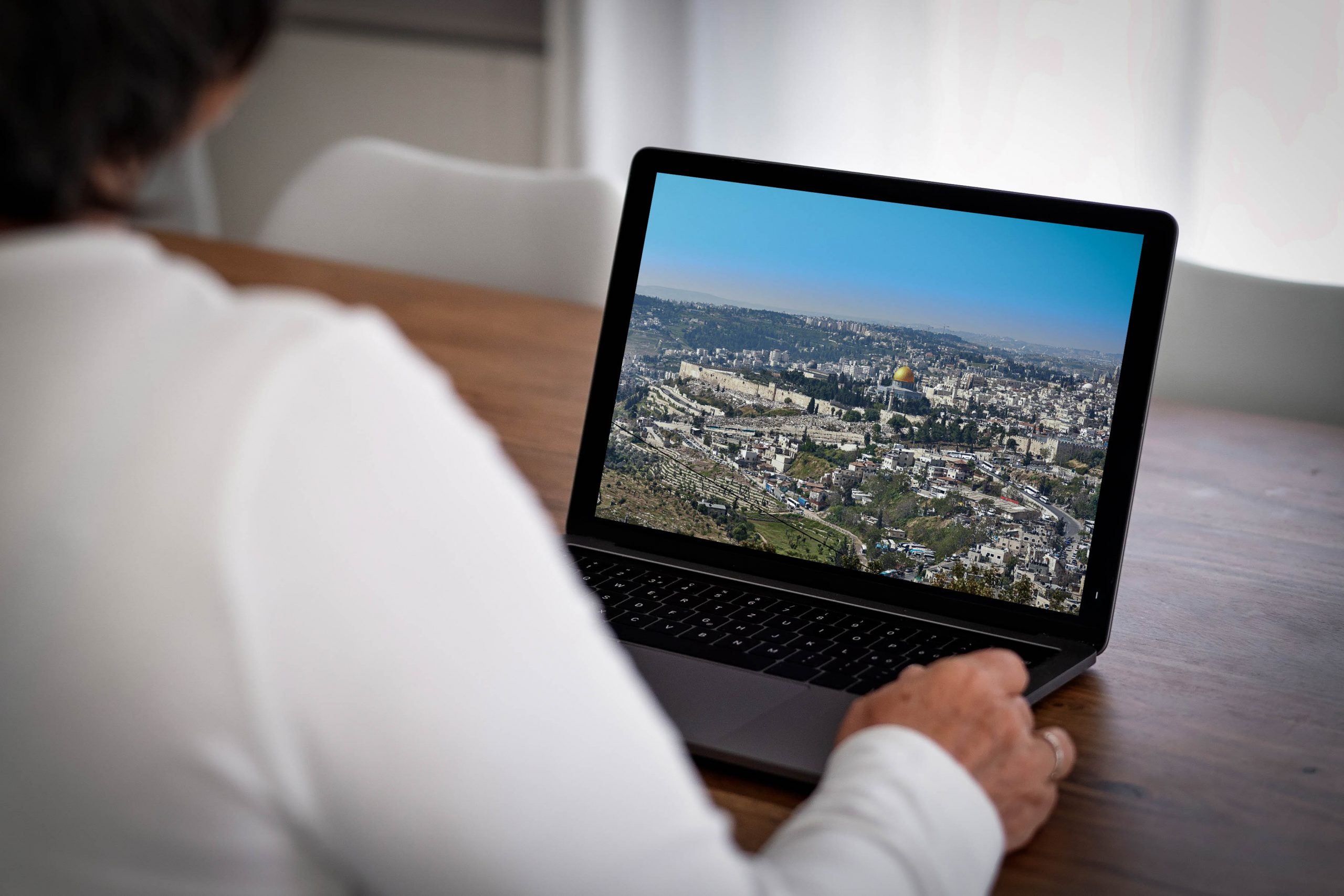 .אישה יושבת מול מחשב נייד ובו תמונה של ירושלים