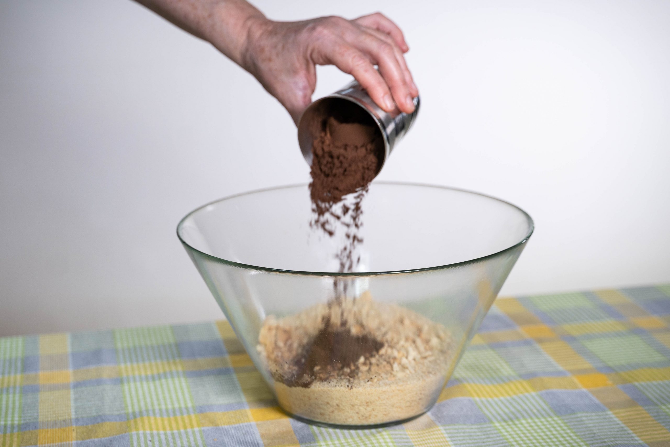 .יד שופכת קקאו מכוס לתוך קערה עם תערובת להכנת כדורי שוקולד
