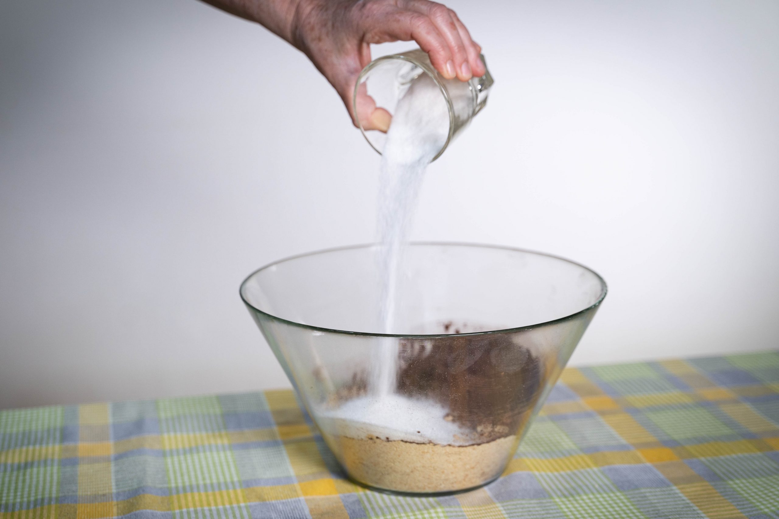 .יד שופכת סוכר מכוס לתוך קערה עם תערובת להכנת כדורי שוקולד