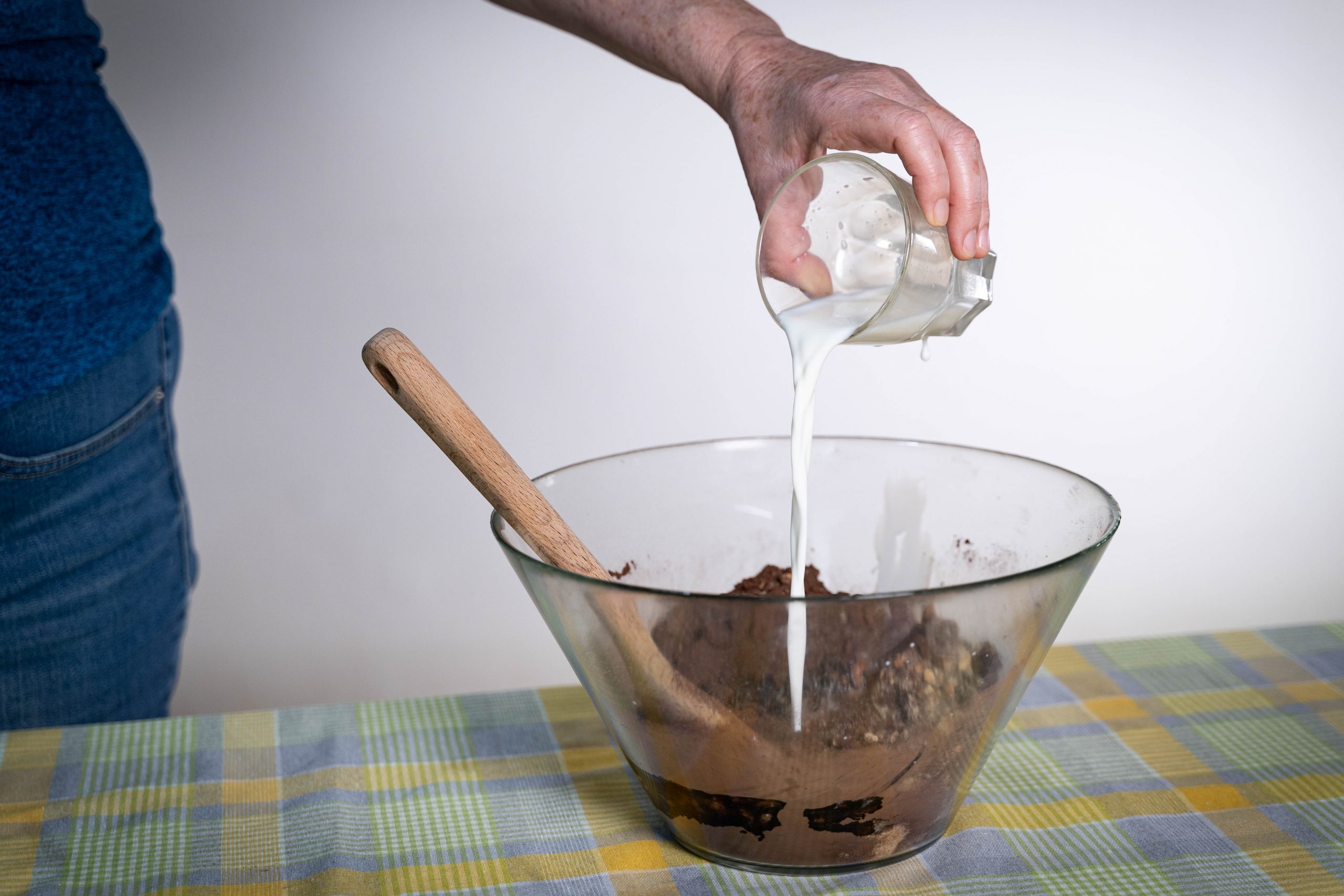 .יד שופכת חלב מכוס לתוך קערה עם תערובת להכנת כדורי שוקולד