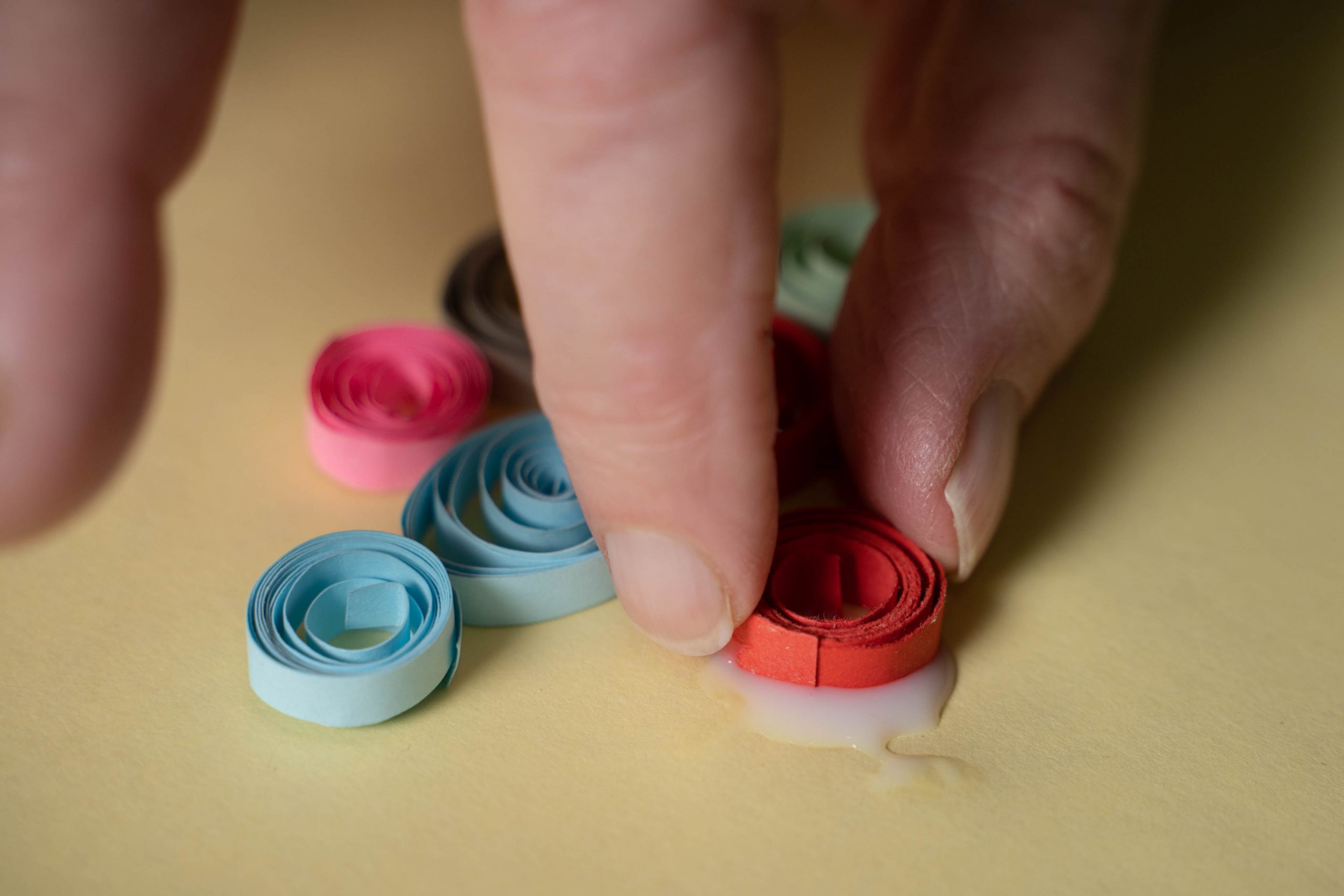 .יד מדביקה נייר צבעוני מגולגל על בריסטול כחלק מיצירת קוולינג