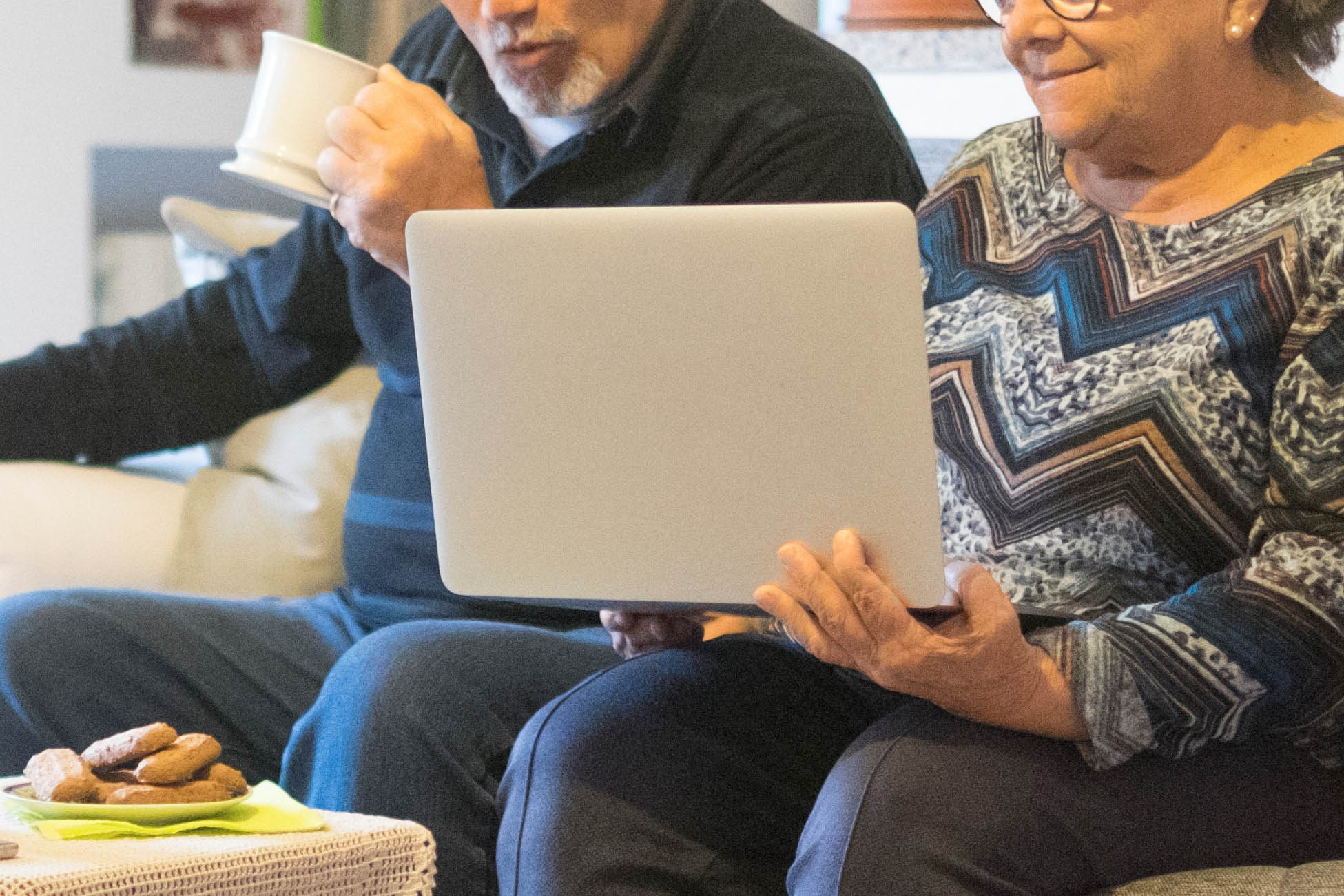 .זוג מבוגרים יושבים על ספה ומסתכלים ביחד במחשב הנייד