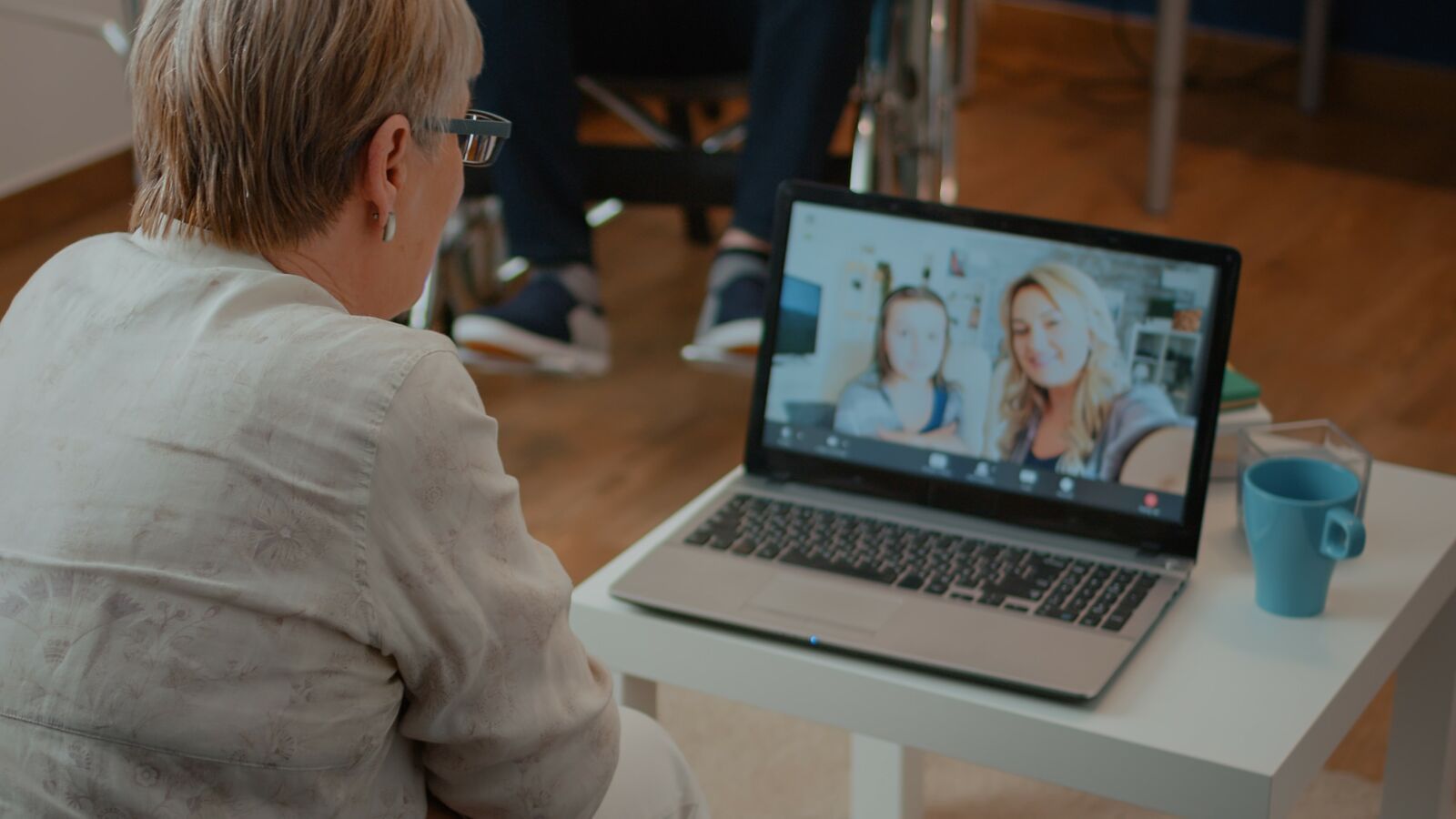 .אישה יושבת מול מסך של מחשב נייד ומשוחחת דרכו עם שתי נשים נוספות, אשר תמונתן מופיעה על המסך